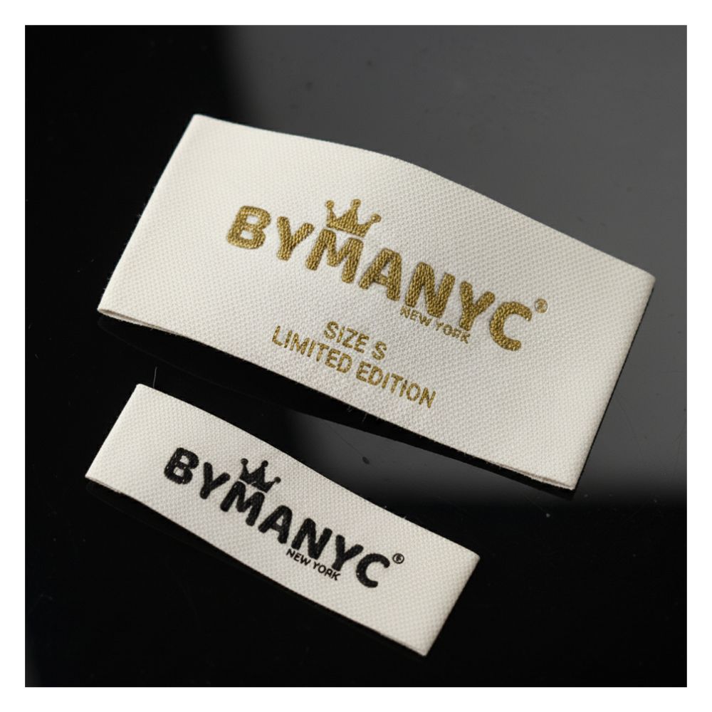 Pair of BYMANYC New York white fabric labels with gold-foil logo and Size S Limited Edition tags.